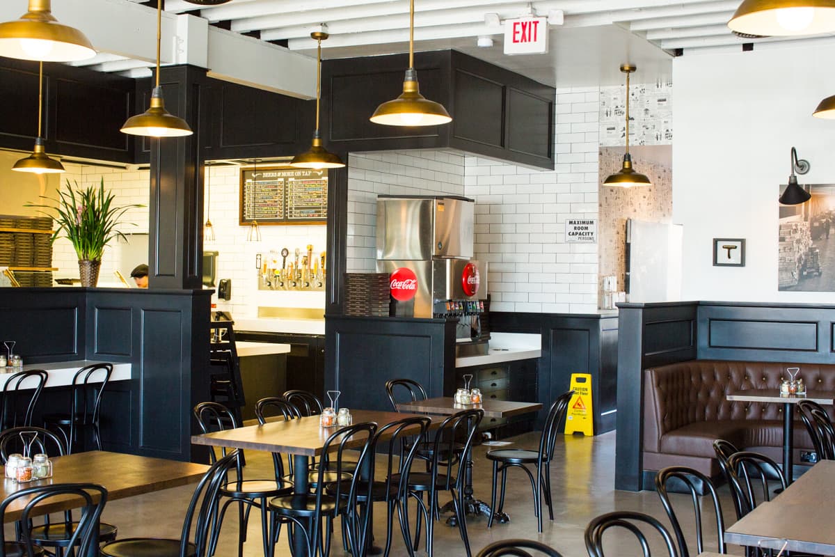 Finished Pizza Press dining room with black bentwood chairs, pendant lights and an open kitchen